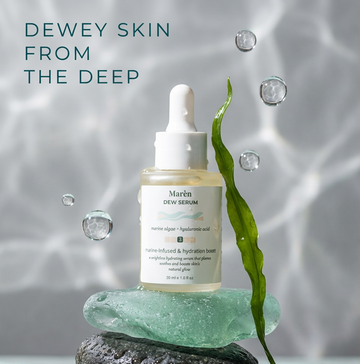 Marèn Dew Serum bottle with marine algae and hyaluronic acid, balanced on wet sea stones with a floating kelp leaf and water bubbles, showcasing a premium hydration treatment for acne-prone and glowing skin.