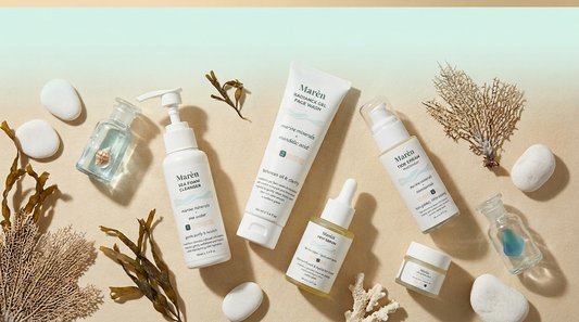 Five Marèn skincare products flat lay — Sea Foam Cleanser, Radiance Gel Face Wash, Dew Serum, Tide Cream, and Lip Quench Balm — arranged on a sandy surface with ocean-inspired props