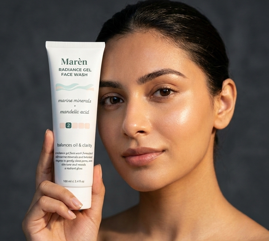 A close-up of a woman with clear dewy skin and wet hair holding a bottle of Marèn Radiance Gel Face Wash in a minimalist setting, representing a refreshing skincare routine for oily skin.