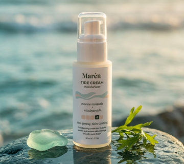 Marèn Tide Cream moisturizer bottle on a coastal rock with sea glass and kelp against a blurred ocean background.
